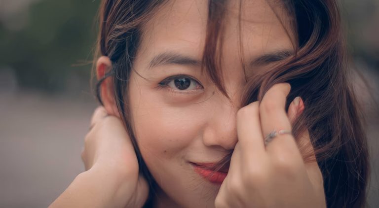Close-up portrait of a young woman with brown hair smiling softly and looking over her shoulder