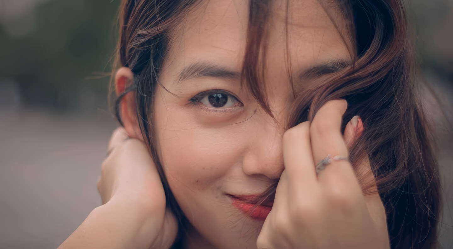 Close-up portrait of a young woman with brown hair smiling softly and looking over her shoulder