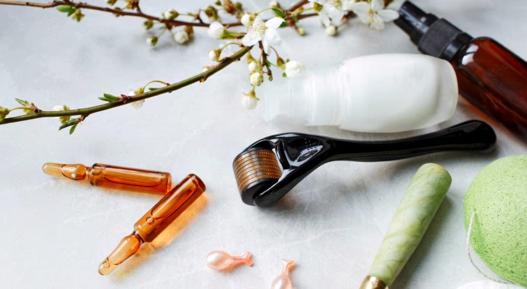 Flat lay of professional skincare tools, glass ampoules, a derma roller, and a jade roller on a white marble surface.