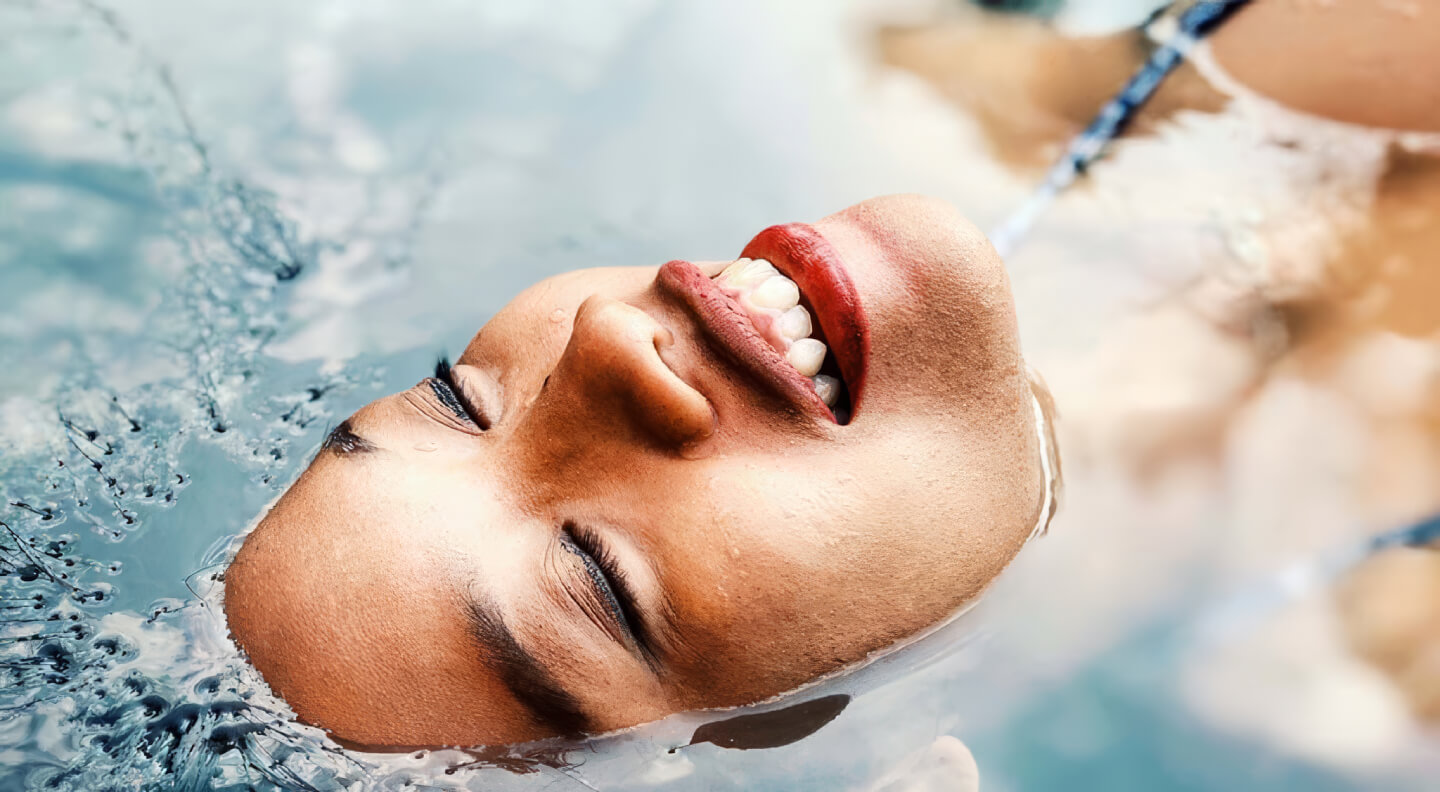 Close-up of a woman’s face floating in clear blue water with bubbles.